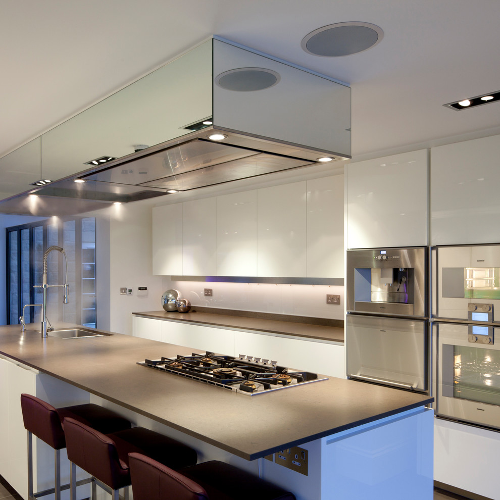 Medium sized contemporary single-wall open plan kitchen in London with flat-panel cabinets, an island, a single-bowl sink, white cabinets, quartz worktops, white splashback, glass sheet splashback, stainless steel appliances, marble flooring, grey floors and grey worktops.