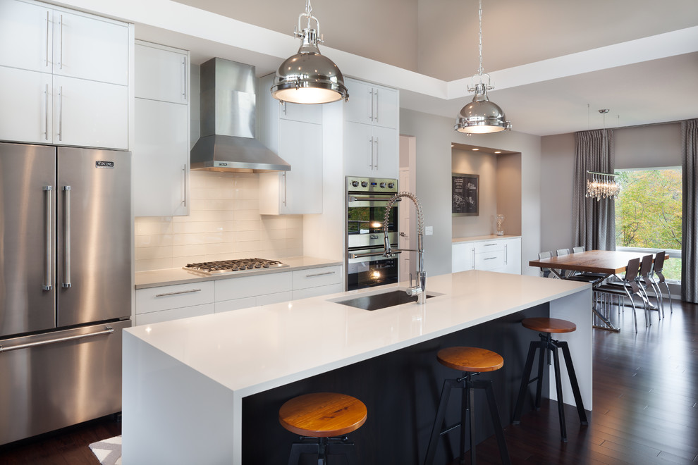 Photo of a contemporary eat-in kitchen in Minneapolis with an undermount sink, flat-panel cabinets, white cabinets, white splashback, stainless steel appliances, dark hardwood floors and with island.