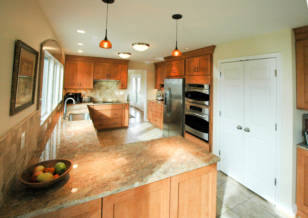 Inspiration for a large transitional l-shaped linoleum floor eat-in kitchen remodel in DC Metro with a farmhouse sink, flat-panel cabinets, light wood cabinets, granite countertops, beige backsplash, stone tile backsplash, stainless steel appliances and a peninsula