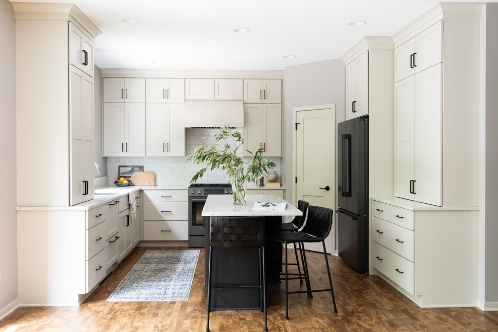Mid-sized transitional u-shaped medium tone wood floor and brown floor eat-in kitchen photo with an undermount sink, shaker cabinets, white cabinets, quartz countertops, white backsplash, subway tile backsplash, black appliances, an island and white countertops