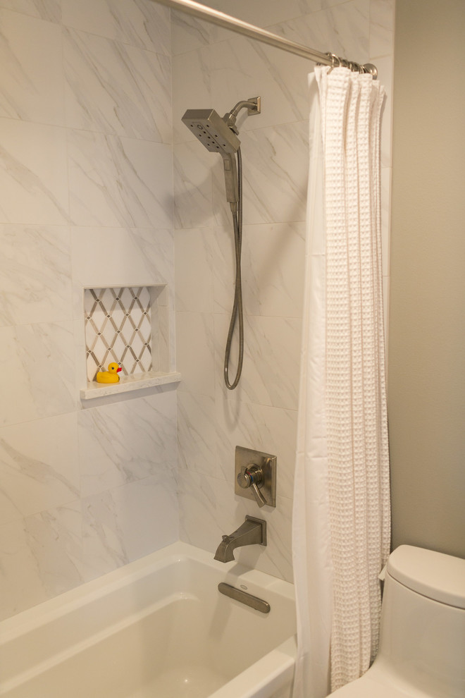 This is an example of a small transitional kids bathroom in Orlando with raised-panel cabinets, grey cabinets, an alcove tub, a shower/bathtub combo, a two-piece toilet, white tile, stone tile, grey walls, marble floors, an undermount sink and engineered quartz benchtops.