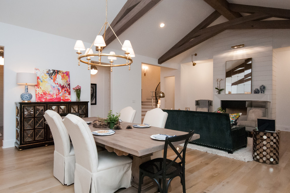 This is an example of a large transitional open plan dining in Houston with white walls, light hardwood floors, a standard fireplace, a wood fireplace surround and beige floor.