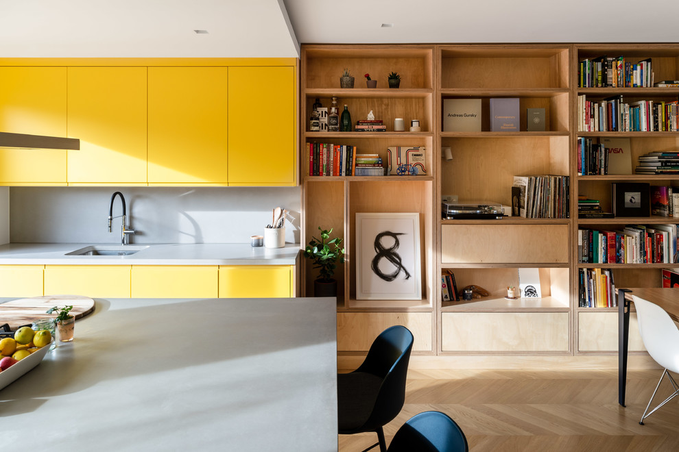 Design ideas for a contemporary kitchen/diner in London with a submerged sink, flat-panel cabinets, yellow cabinets, grey splashback, light hardwood flooring, an island, beige floors and grey worktops.