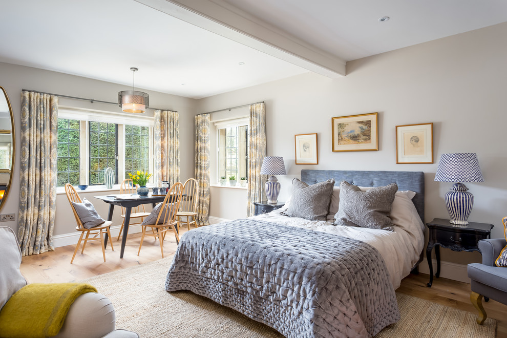 This is an example of a large traditional master bedroom in Gloucestershire with grey walls, medium hardwood floors, a wood stove and a stone fireplace surround.