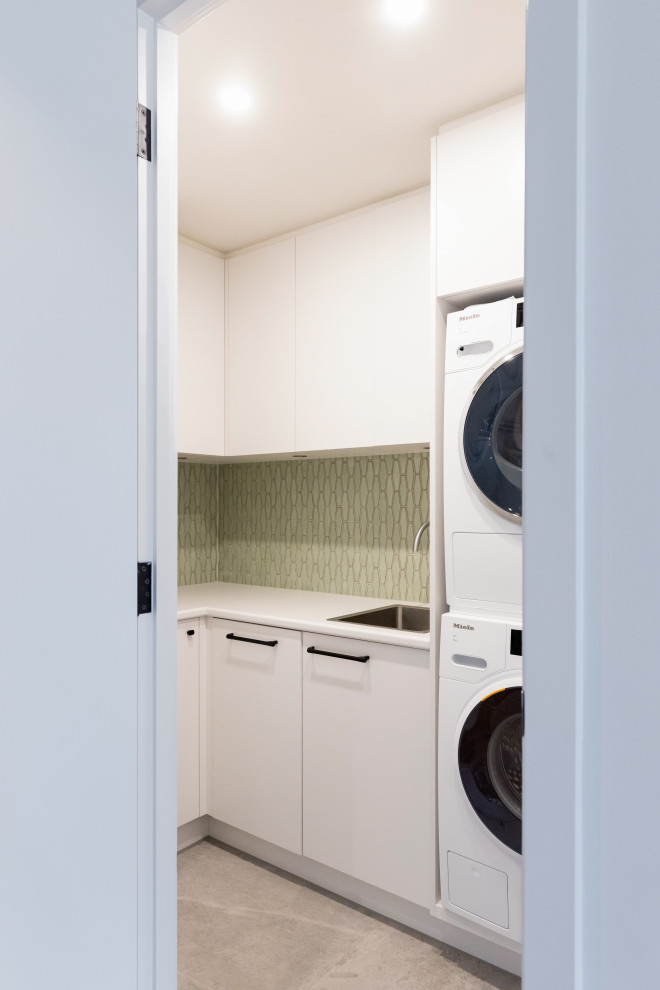 Ispirazione per una piccola sala lavanderia design con lavello a vasca singola, ante lisce, ante bianche, top in laminato, paraspruzzi verde, paraspruzzi con piastrelle in ceramica, pareti bianche, lavatrice e asciugatrice a colonna, top bianco, pavimento in gres porcellanato e pavimento grigio