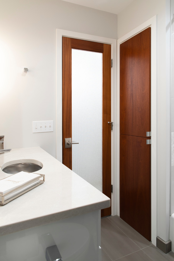 Photo of a small midcentury bathroom in Omaha with flat-panel cabinets, white cabinets, quartzite benchtops, white benchtops, an alcove tub, a shower/bathtub combo, a one-piece toilet, multi-coloured tile, ceramic tile, grey walls, porcelain floors, an undermount sink, grey floor and a shower curtain.