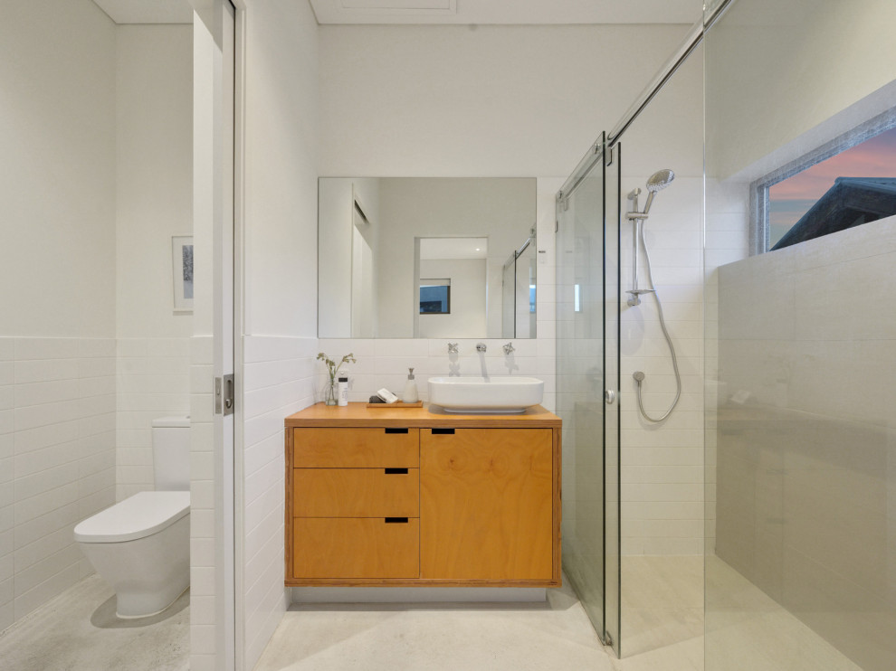 Midcentury 3/4 bathroom in Perth with flat-panel cabinets, light wood cabinets, a curbless shower, a one-piece toilet, white tile, white walls, a vessel sink, wood benchtops, beige floor, a sliding shower screen, an enclosed toilet, a single vanity and a floating vanity.