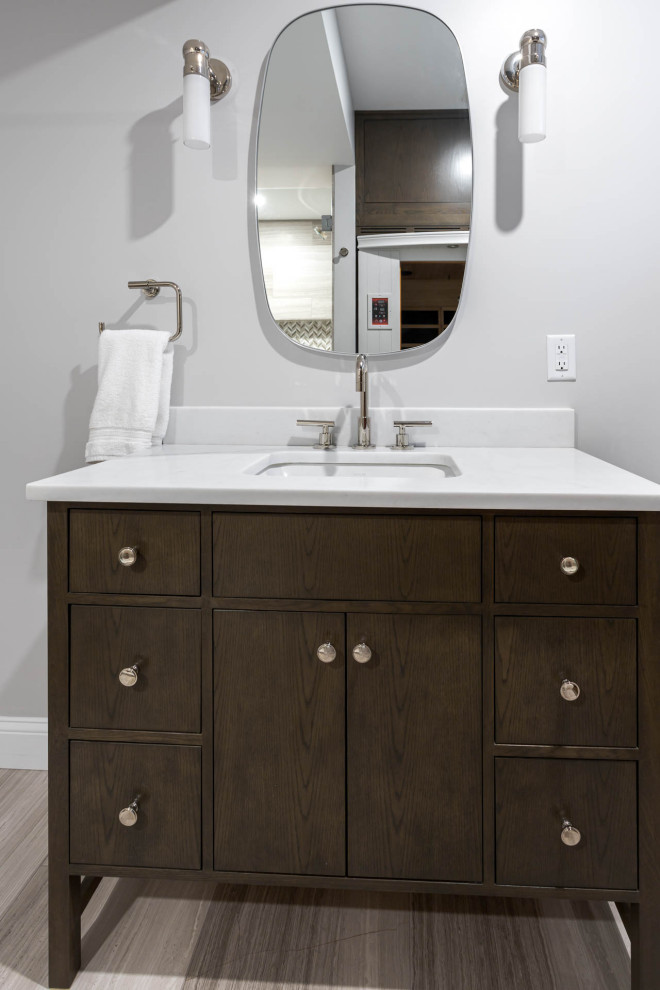 This is an example of a mid-sized transitional bathroom in Denver with beaded inset cabinets, medium wood cabinets, an open shower, a two-piece toilet, gray tile, limestone, grey walls, marble floors, with a sauna, an undermount sink, quartzite benchtops, grey floor, a hinged shower door, white benchtops, a single vanity and a freestanding vanity.