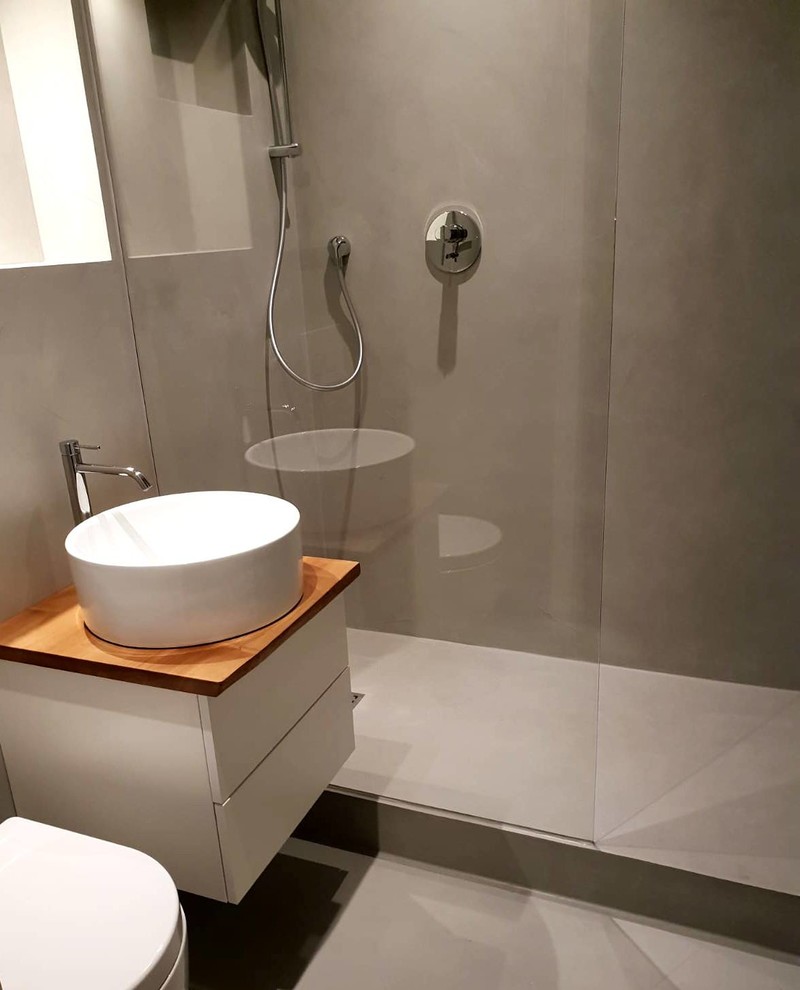 Duschbad mit Kassettenfronten, weißen Schränken, offener Dusche, Wandtoilette, grauer Wandfarbe, Betonboden, Aufsatzwaschbecken, Waschtisch aus Holz, grauem Boden und brauner Waschtischplatte in Hamburg