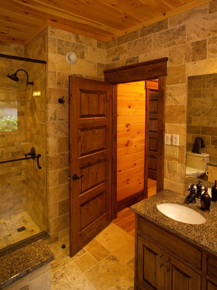 Mid-sized country master bathroom in Ottawa with raised-panel cabinets, medium wood cabinets, an alcove shower, a two-piece toilet, multi-coloured tile, stone tile, an undermount sink, brown floor, a hinged shower door, multi-coloured walls and travertine floors.