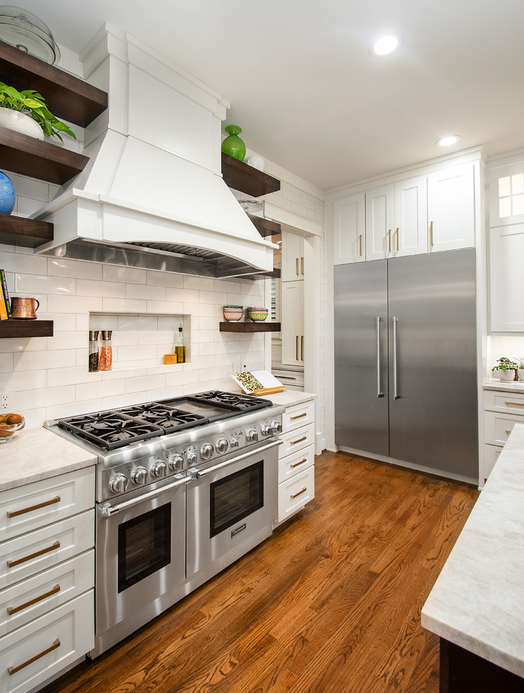 Inspiration for a large transitional l-shaped open plan kitchen in Dallas with a drop-in sink, flat-panel cabinets, white cabinets, quartzite benchtops, white splashback, ceramic splashback, stainless steel appliances, dark hardwood floors, with island, brown floor and grey benchtop.