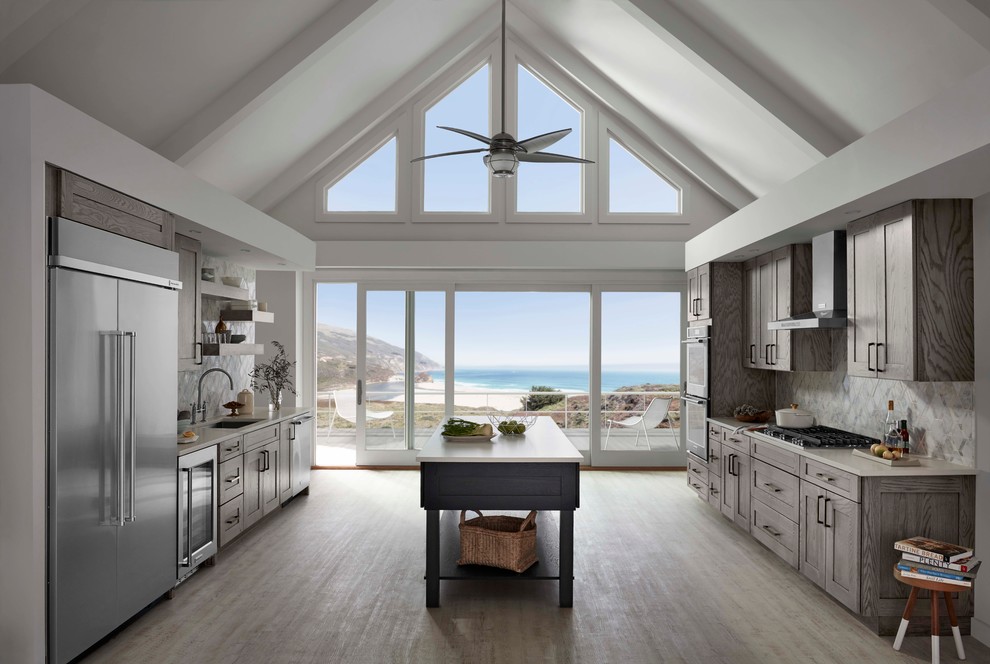 Inspiration for a mid-sized beach style galley open plan kitchen in Minneapolis with grey cabinets, an undermount sink, shaker cabinets, quartz benchtops, multi-coloured splashback, stone tile splashback, stainless steel appliances, light hardwood floors and with island.