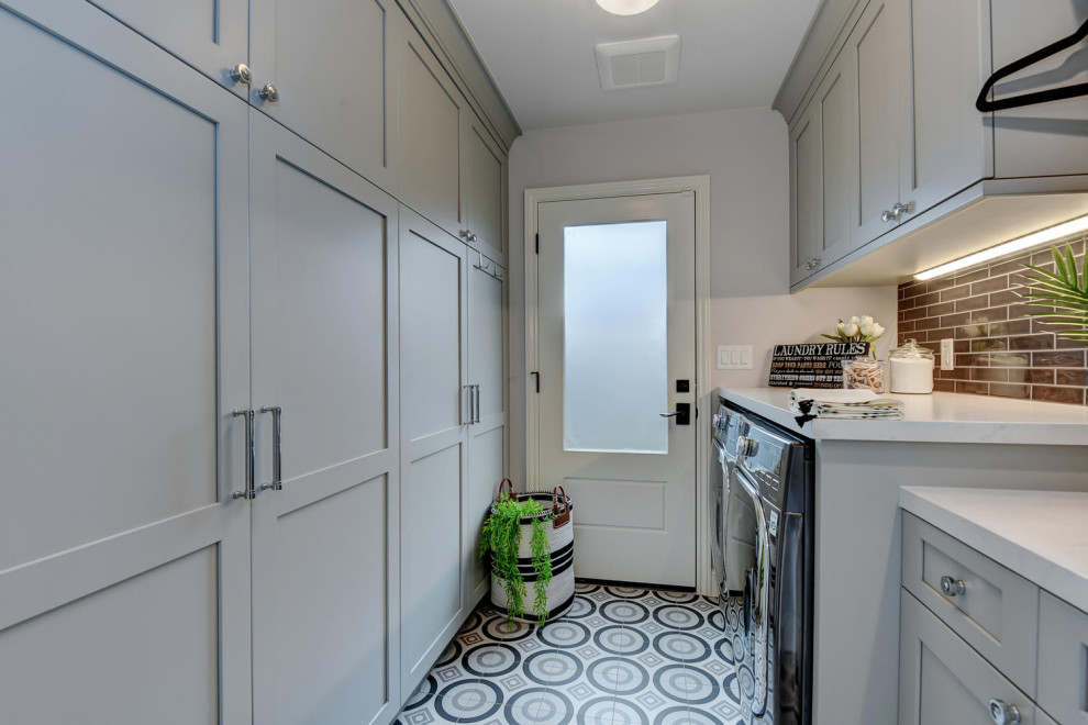 This is an example of a mid-sized contemporary galley dedicated laundry room in San Francisco with an undermount sink, raised-panel cabinets, grey cabinets, quartz benchtops, grey walls, ceramic floors, a side-by-side washer and dryer, multi-coloured floor, grey benchtop, black splashback and glass sheet splashback.