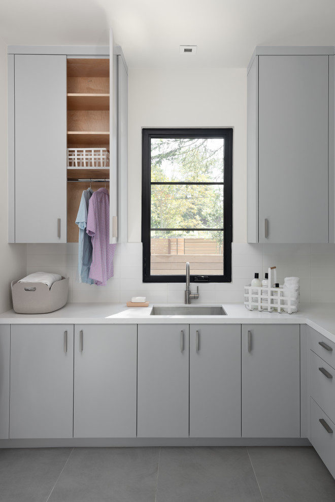 Example of a trendy porcelain tile and gray floor laundry room design in San Francisco with an undermount sink, flat-panel cabinets, gray cabinets, quartz countertops, white backsplash, ceramic backsplash, white walls and white countertops