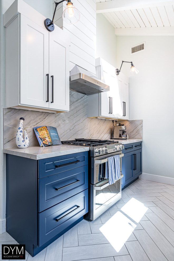 Example of a beach style galley white floor, vaulted ceiling and light wood floor eat-in kitchen design in Los Angeles with a farmhouse sink, shaker cabinets, blue cabinets, quartz countertops, white backsplash, quartz backsplash, stainless steel appliances, a peninsula and white countertops