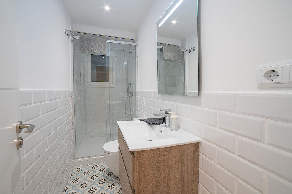 This is an example of a mid-sized contemporary master bathroom in Barcelona with flat-panel cabinets, medium wood cabinets, a curbless shower, a one-piece toilet, white tile, ceramic tile, white walls, ceramic floors, a trough sink, beige floor, a sliding shower screen, white benchtops, a single vanity and a floating vanity.