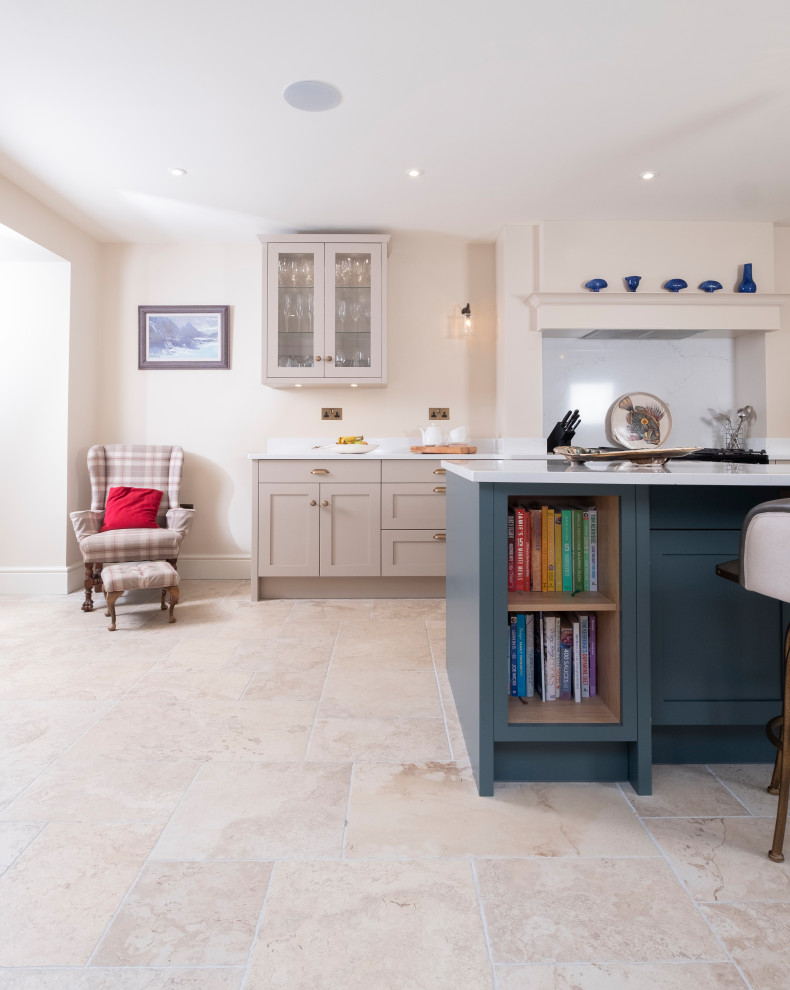 This is an example of a large traditional single-wall open plan kitchen in Cardiff with a farmhouse sink, shaker cabinets, quartzite benchtops, limestone floors, with island and white benchtop.