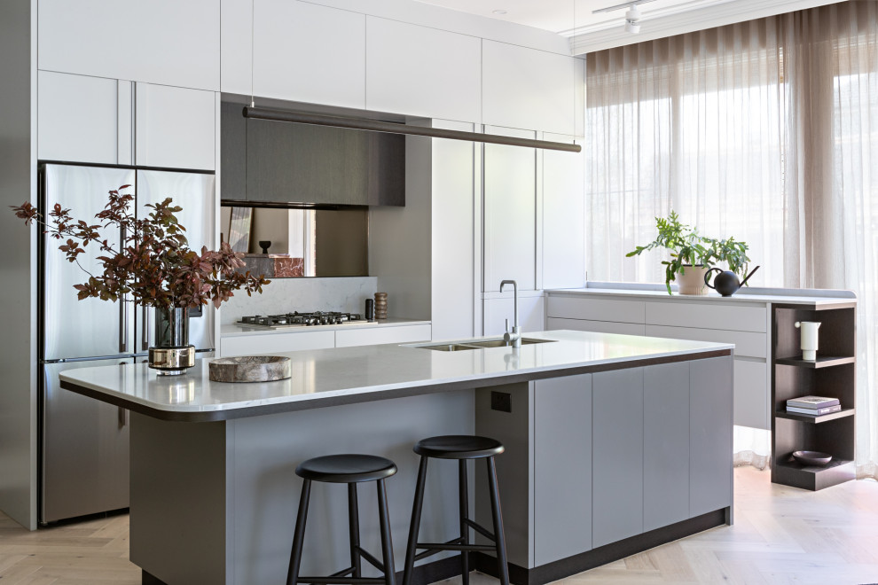 This is an example of a contemporary l-shaped kitchen in Melbourne with an undermount sink, flat-panel cabinets, white cabinets, stainless steel appliances, light hardwood floors, with island, beige floor and white benchtop.