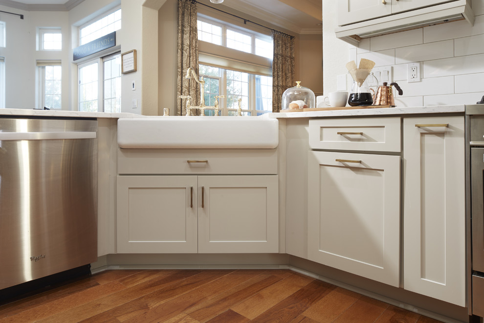 Mid-sized transitional u-shaped medium tone wood floor and brown floor enclosed kitchen photo in Atlanta with a farmhouse sink, shaker cabinets, gray cabinets, quartz countertops, white backsplash, subway tile backsplash, stainless steel appliances, a peninsula and white countertops