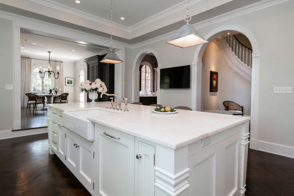 This is an example of a transitional eat-in kitchen in Baltimore with a farmhouse sink, shaker cabinets, white cabinets, marble benchtops, dark hardwood floors, with island, brown floor, white benchtop and recessed.