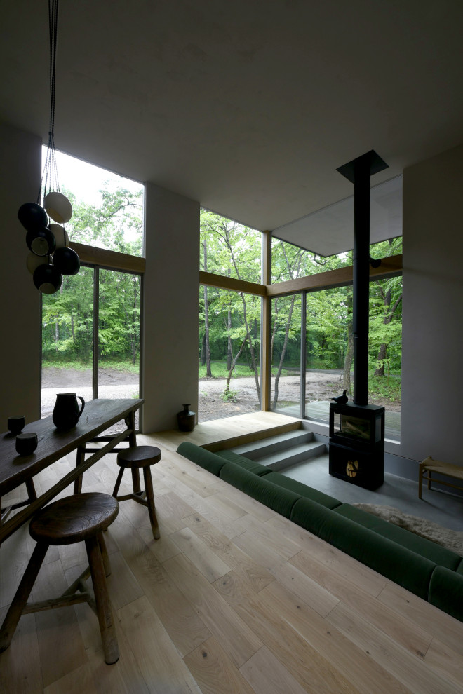 Foto de salón abierto de tamaño medio sin televisor con paredes grises, suelo de madera clara, estufa de leña, marco de chimenea de hormigón y suelo gris