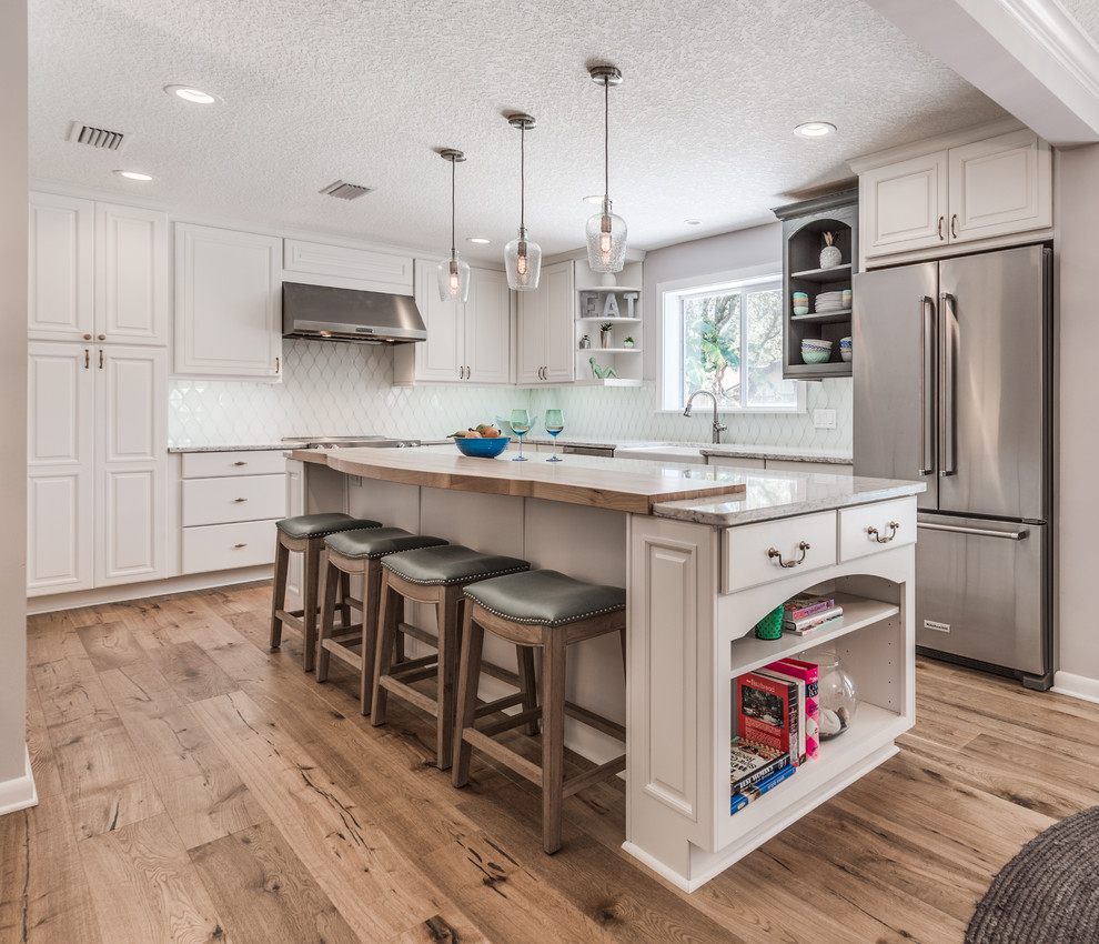 Photo of a transitional eat-in kitchen in Jacksonville with a farmhouse sink, raised-panel cabinets, white cabinets, quartz benchtops, white splashback, glass tile splashback, stainless steel appliances, medium hardwood floors and with island.