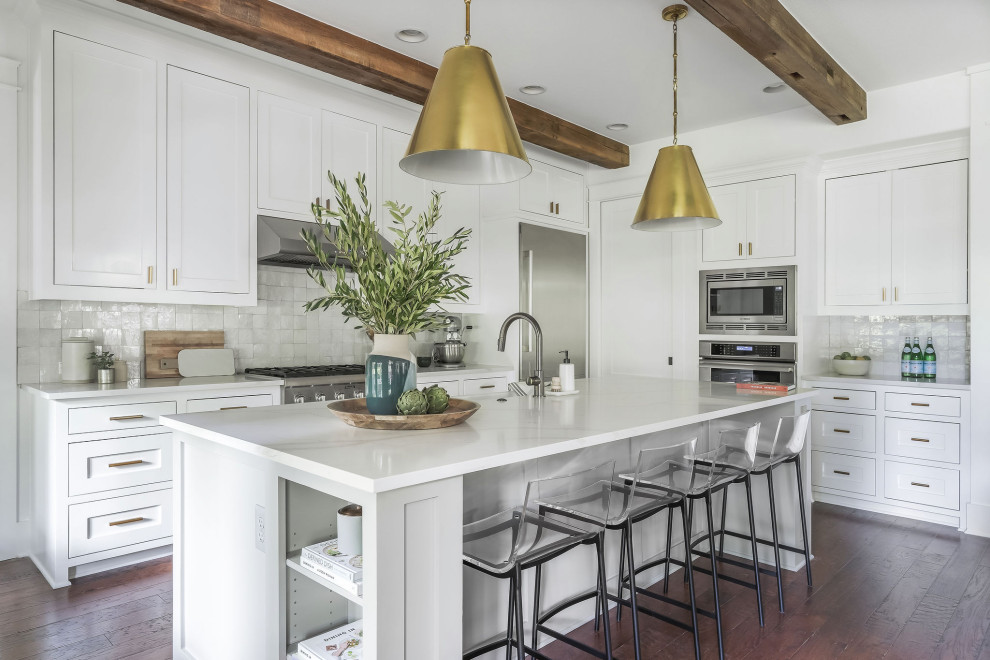 Inspiration for a medium sized modern l-shaped kitchen in Austin with a belfast sink, shaker cabinets, white cabinets, engineered stone countertops, white splashback, stainless steel appliances, dark hardwood flooring, an island, brown floors, white worktops and exposed beams.