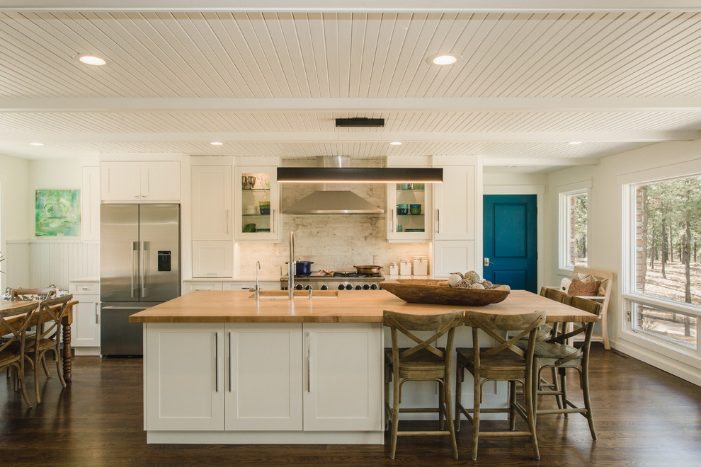 Eat-in kitchen - large coastal galley brown floor and dark wood floor eat-in kitchen idea in Denver with shaker cabinets, white cabinets, porcelain backsplash, stainless steel appliances, an island, an undermount sink, wood countertops, gray backsplash and beige countertops