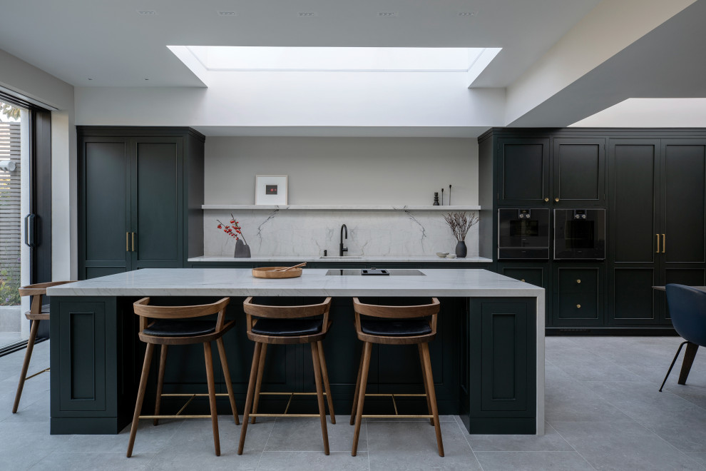 This is an example of a traditional galley kitchen in Dublin with recessed-panel cabinets, black cabinets, white splashback, stone slab splashback, black appliances, an island, grey floors and white worktops.