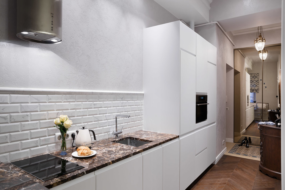 Inspiration for a small transitional single-wall kitchen in Saint Petersburg with an undermount sink, white cabinets, marble benchtops, white splashback, ceramic splashback, dark hardwood floors, black appliances and brown floor.
