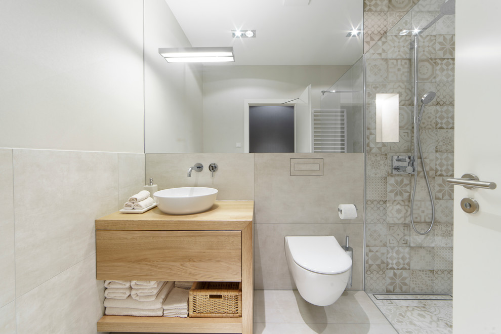 This is an example of a mid-sized powder room in Leipzig with medium wood cabinets, a wall-mount toilet, beige tile, a vessel sink, wood benchtops, beige floor, open cabinets, ceramic tile, beige walls and ceramic floors.