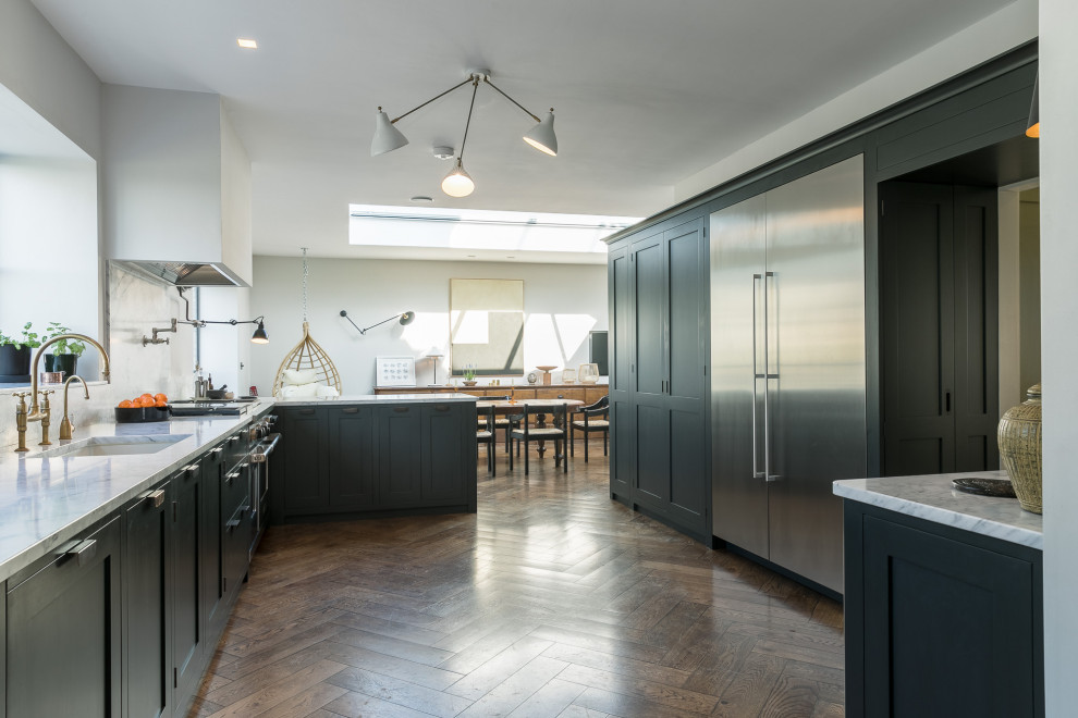 Photo of a large arts and crafts galley eat-in kitchen in Other with a drop-in sink, dark wood cabinets, marble benchtops, white splashback, marble splashback, panelled appliances, dark hardwood floors, a peninsula, brown floor and white benchtop.