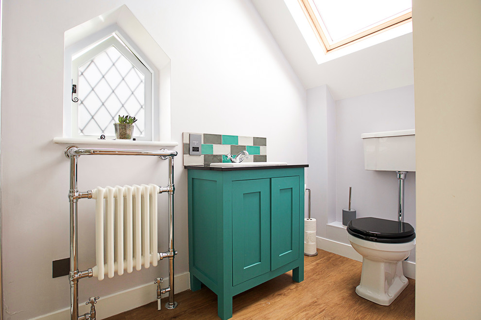 Design ideas for a midcentury powder room in London with shaker cabinets, turquoise cabinets, a two-piece toilet, grey walls, medium hardwood floors, a console sink and brown floor.
