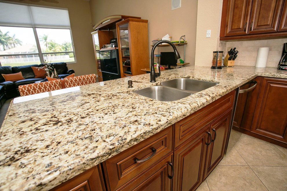 Mid-sized transitional u-shaped porcelain tile eat-in kitchen photo in Miami with an undermount sink, raised-panel cabinets, brown cabinets, granite countertops, beige backsplash, stone tile backsplash, stainless steel appliances, beige walls and a peninsula
