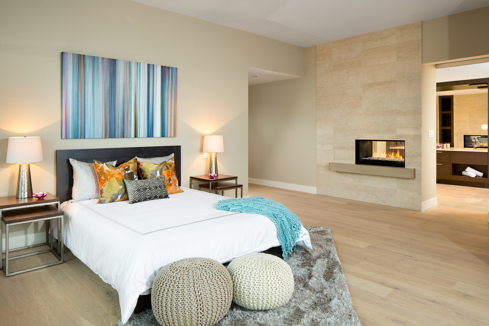 This is an example of a contemporary master bedroom in Vancouver with a stone fireplace surround, beige walls, light hardwood floors and a two-sided fireplace.