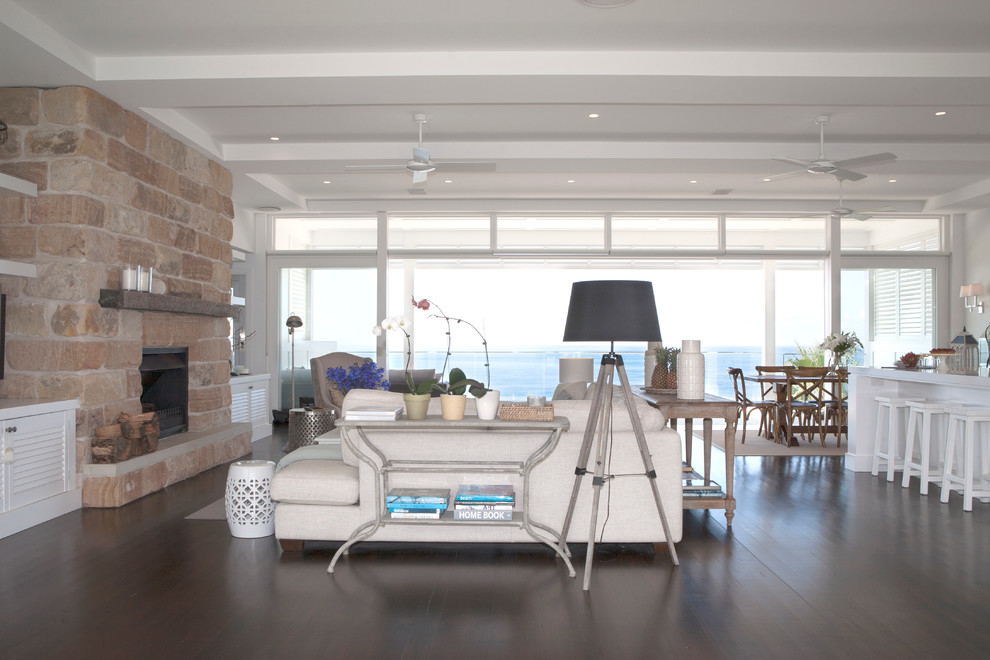 Inspiration for a large beach style open concept living room in Sydney with white walls, dark hardwood floors, a standard fireplace, a stone fireplace surround and a wall-mounted tv.