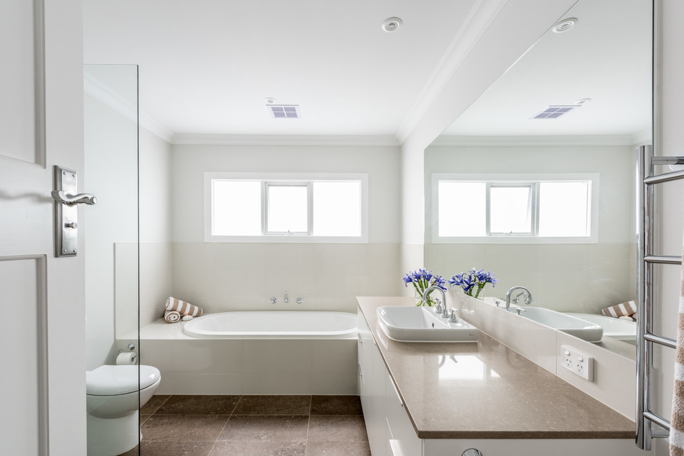 Photo of a mid-sized modern 3/4 bathroom in Melbourne with white cabinets, beige tile, a one-piece toilet, porcelain tile, porcelain floors, an open shower, flat-panel cabinets, a drop-in tub, grey walls, an integrated sink and engineered quartz benchtops.