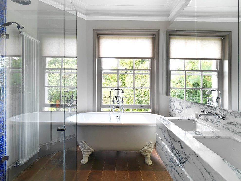 Photo of a mid-sized eclectic master bathroom in London with glass-front cabinets, white cabinets, a claw-foot tub, a corner shower, a wall-mount toilet, blue tile, mosaic tile, grey walls, dark hardwood floors, an undermount sink and marble benchtops.