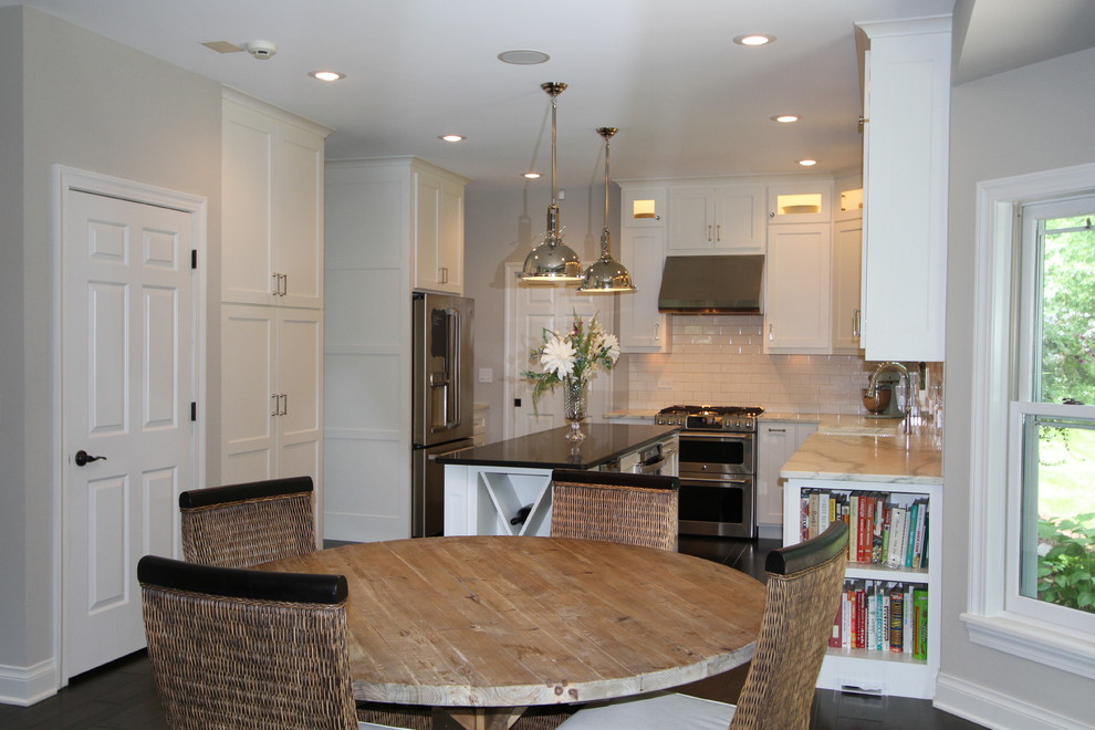 Transitional dark wood floor eat-in kitchen photo with a farmhouse sink, flat-panel cabinets, white cabinets, marble countertops, white backsplash, subway tile backsplash, stainless steel appliances and an island