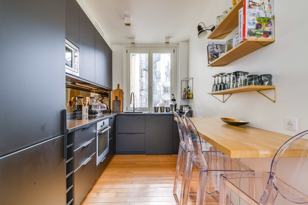 Design ideas for a contemporary l-shaped eat-in kitchen in Paris with an integrated sink, flat-panel cabinets, black cabinets, stainless steel appliances, medium hardwood floors, no island, beige floor and black benchtop.