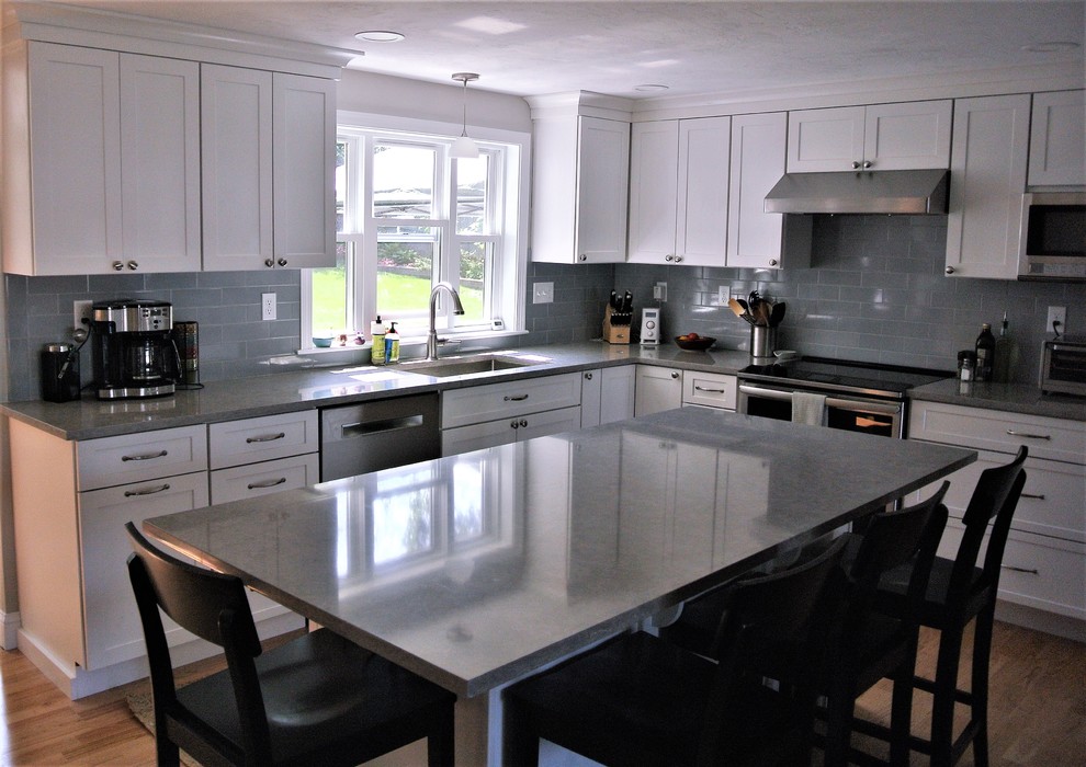 Example of a transitional light wood floor kitchen design in Boston with an undermount sink, shaker cabinets, white cabinets, quartz countertops, gray backsplash, subway tile backsplash, stainless steel appliances, an island and gray countertops