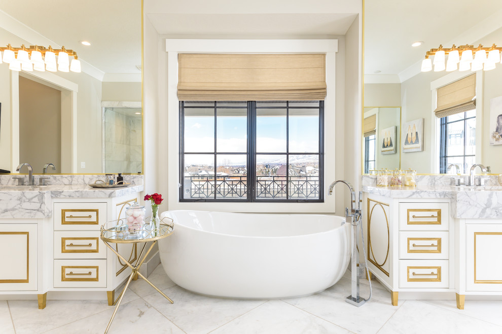 Photo of an expansive transitional master bathroom in Salt Lake City with white cabinets, a freestanding tub, white floor, raised-panel cabinets, beige walls, marble floors, an integrated sink, marble benchtops and grey benchtops.