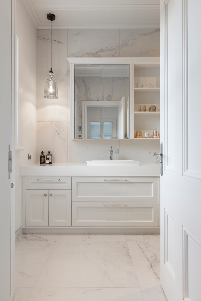 This is an example of a large transitional 3/4 bathroom in Hamilton with recessed-panel cabinets, white cabinets, a corner shower, a wall-mount toilet, white tile, a drop-in sink, solid surface benchtops, stone tile, multi-coloured walls and marble floors.