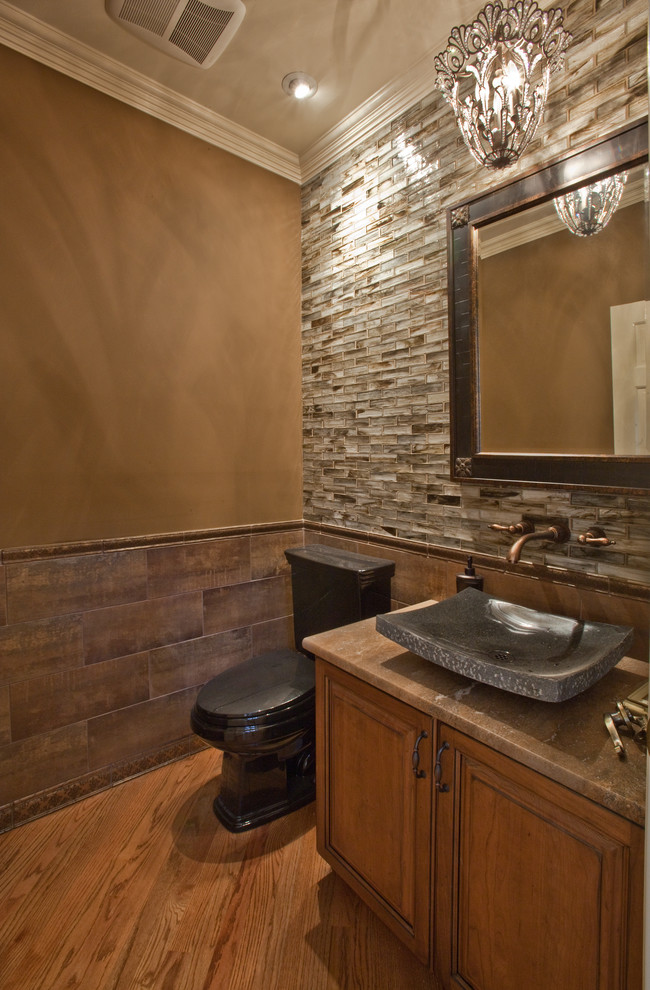 Inspiration for a traditional powder room in Seattle with a vessel sink, raised-panel cabinets, medium wood cabinets, travertine benchtops, a two-piece toilet and brown tile.