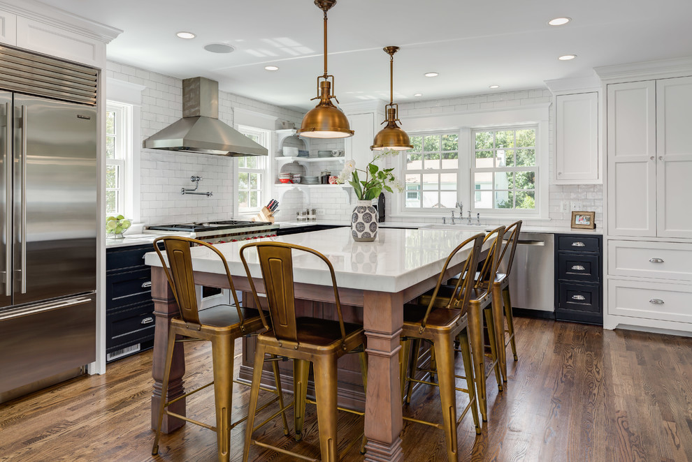 Inspiration for a large transitional l-shaped open plan kitchen in DC Metro with a farmhouse sink, shaker cabinets, white cabinets, quartz benchtops, white splashback, subway tile splashback, stainless steel appliances, medium hardwood floors, with island, brown floor and white benchtop.