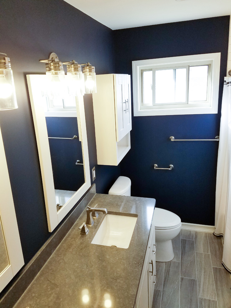 Photo of a small transitional kids bathroom in Detroit with shaker cabinets, white cabinets, an alcove tub, a two-piece toilet, white tile, subway tile, blue walls, ceramic floors, an undermount sink, engineered quartz benchtops and grey floor.