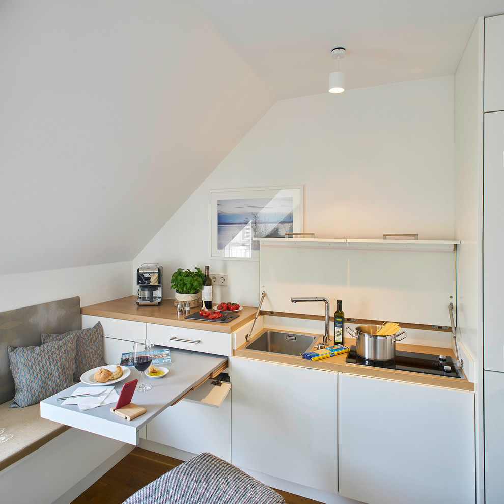 This is an example of a small contemporary single-wall eat-in kitchen in Stuttgart with flat-panel cabinets, white cabinets, laminate benchtops, white splashback, panelled appliances, medium hardwood floors, beige benchtop, an undermount sink and brown floor.