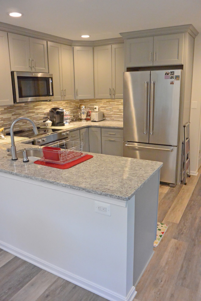 Small transitional u-shaped eat-in kitchen in DC Metro with an undermount sink, shaker cabinets, grey cabinets, granite benchtops, grey splashback, mosaic tile splashback, stainless steel appliances, vinyl floors, a peninsula, brown floor and grey benchtop.