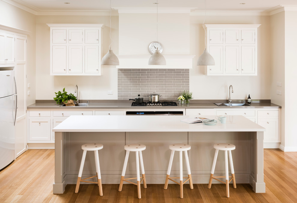 Transitional kitchen in Melbourne with a drop-in sink, shaker cabinets, white cabinets, white appliances, medium hardwood floors, with island, grey splashback and subway tile splashback.