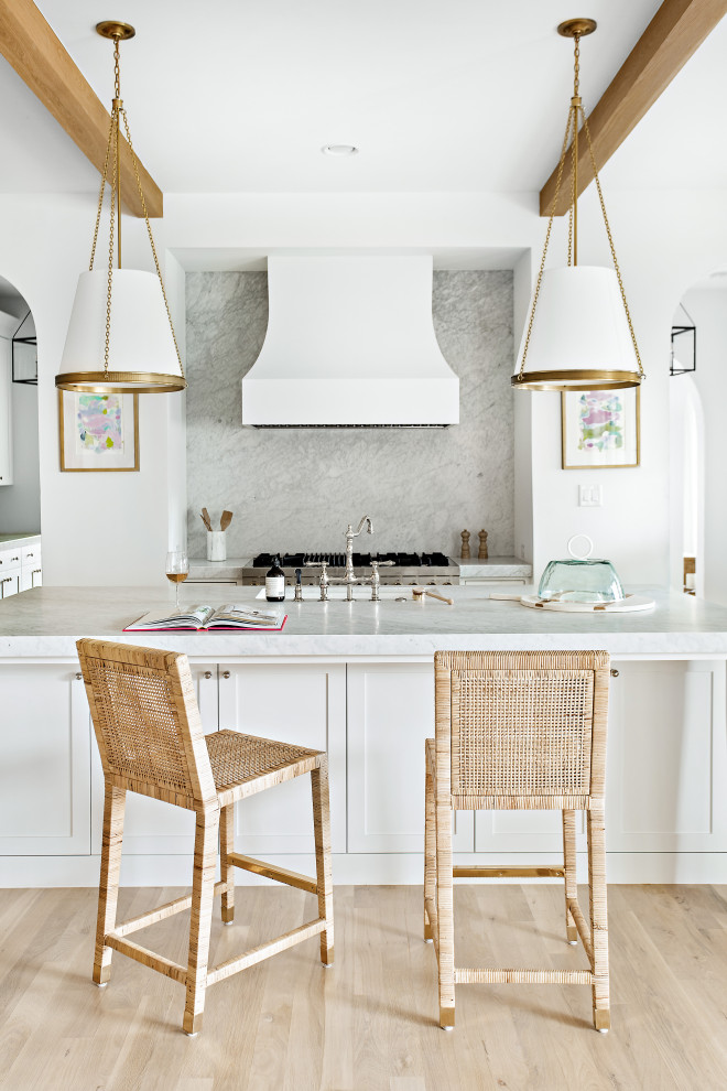 Inspiration for a large transitional l-shaped open plan kitchen in Dallas with an undermount sink, shaker cabinets, white cabinets, marble benchtops, white splashback, marble splashback, panelled appliances, light hardwood floors, with island, brown floor, white benchtop and exposed beam.